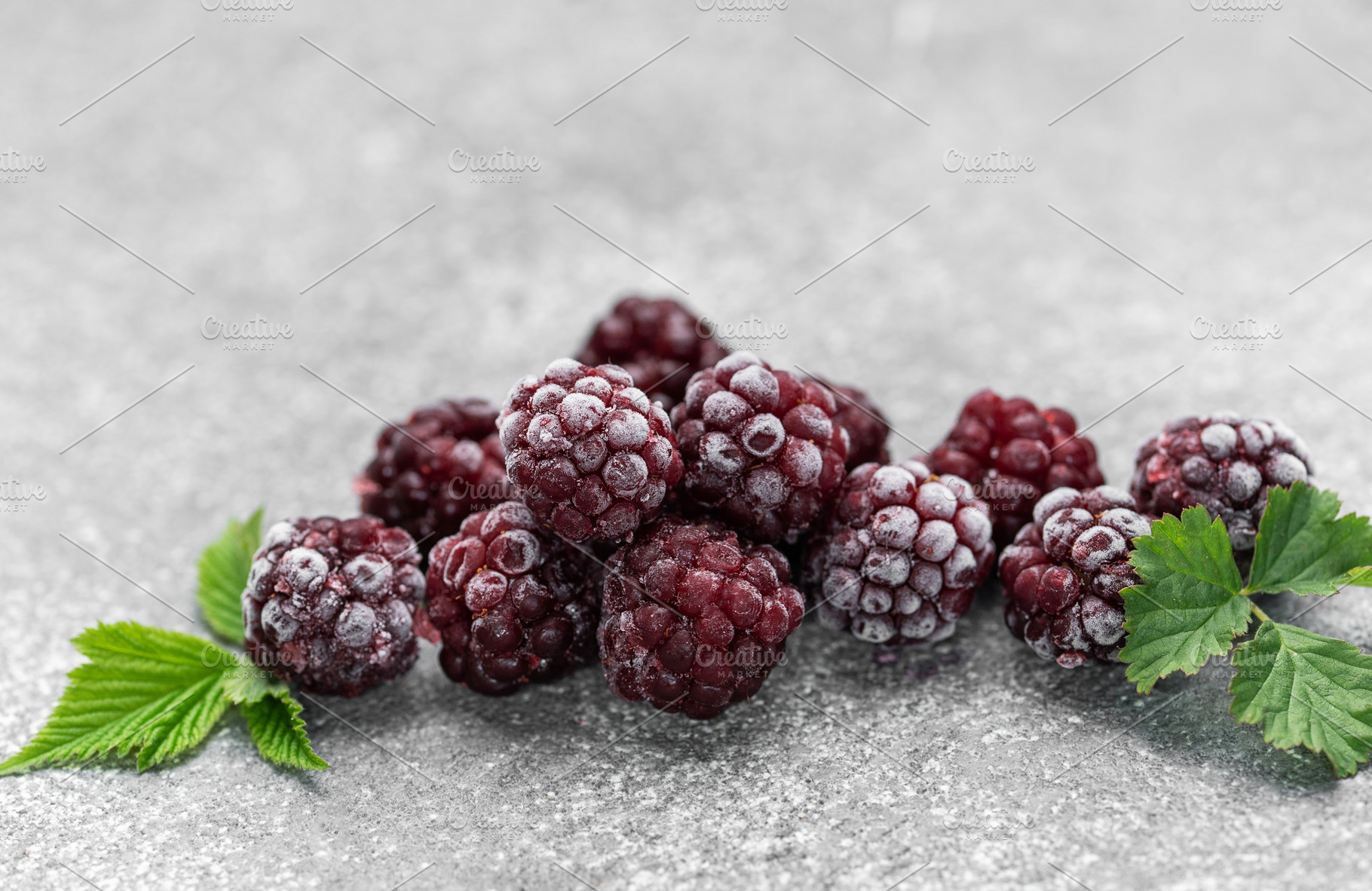 Frozen blackberries with green leaves on gray background, a Food & Drink Photo by Olena Rudo