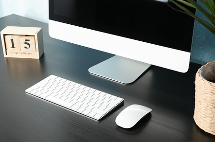Workplace with computer, plant and calendar on black wood table,, a Business Photo by AtlasStudio