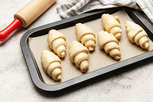 Raw croissants baking on tray with rolling pin and kitchen towel, a Food & Drink Photo by Olena Rudo