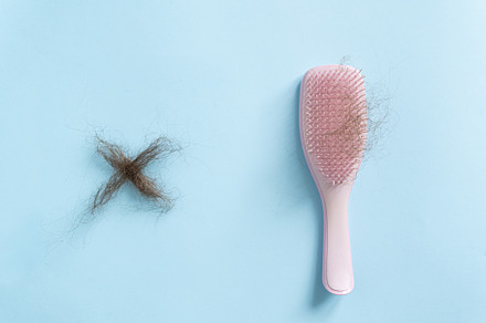 Hair loss concept - pink brush with lost hair and cross made of lost hair