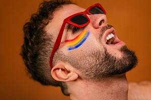 Man expressing pride wearing rainbow face paint and red sunglasses, a Photo by karrastock