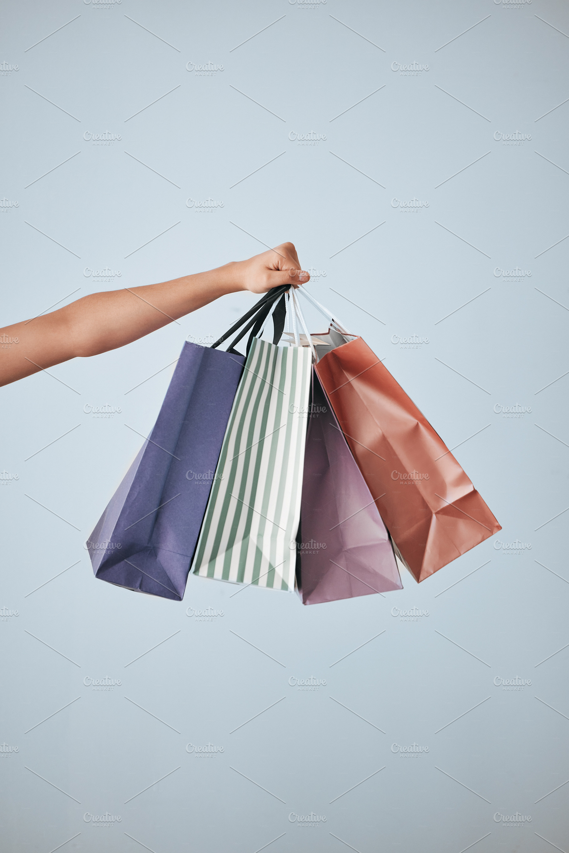 Hands, shopping bags and purchase on mockup in sale, discount or fashion against a gray studio background. Hand of shopper holding bag of gifts, present or luxury retail products on copy space, a Photo by Peopleimages.com