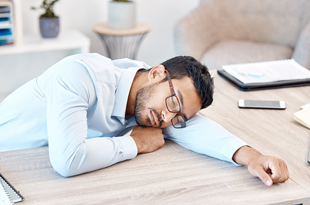 Burnout, sleeping and tired with an overworked business man asleep at his desk in the office. Exhausted, fatigue and dreaming with a young male employee napping on a table at work after working late, a Photo by Peopleimages.com