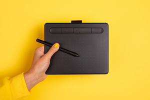 Hand holding pen and digital drawing tablet against vibrant yell, a Technology Photo by Ales Munt