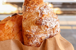Croissant and pastry in paper bag, holding fresh baked food at train station, e, a Photo by Studio ANNA