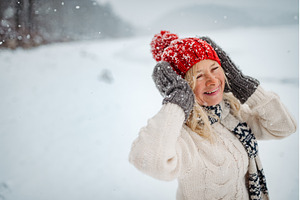 Senior woman enjoying snowfall in, a Holiday Photo by HalfPoint