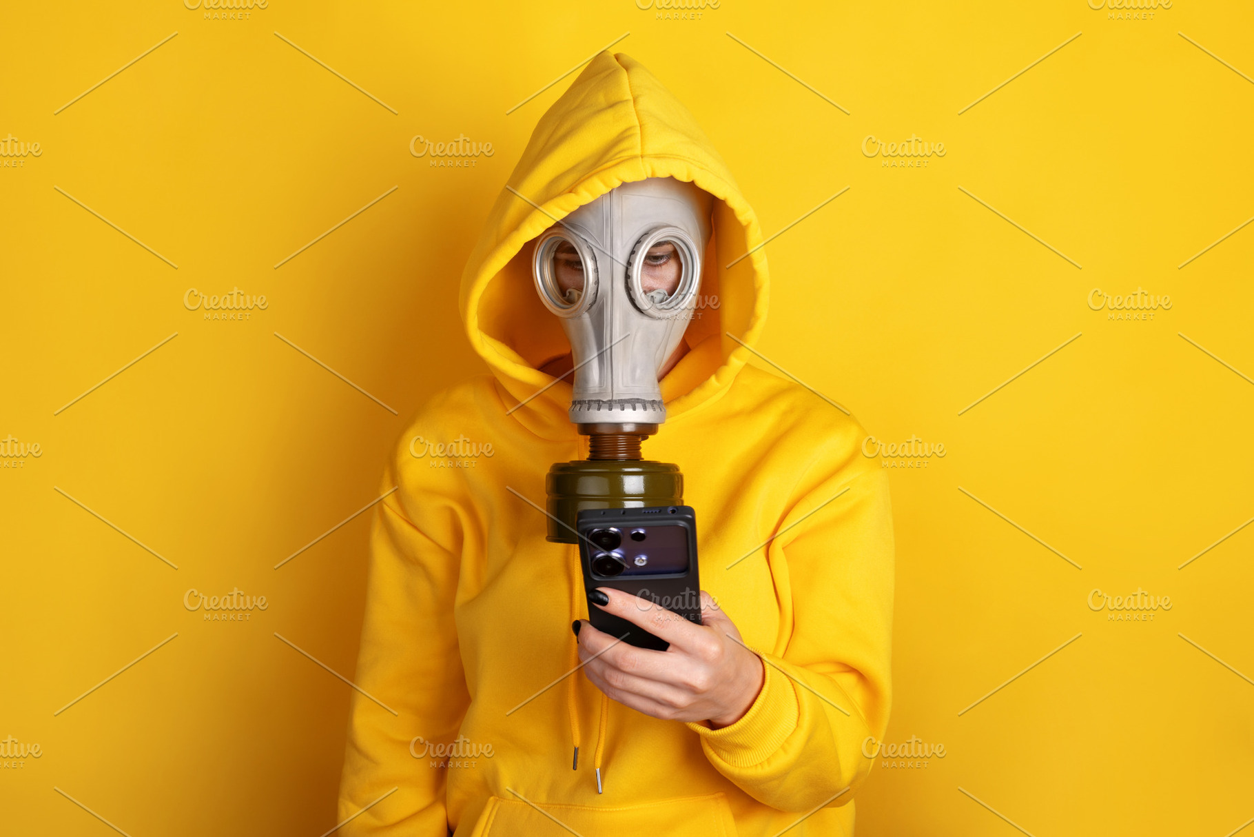 Individual in yellow hoodie and gas mask holding smartphone agai, a Person Photo by Ales Munt