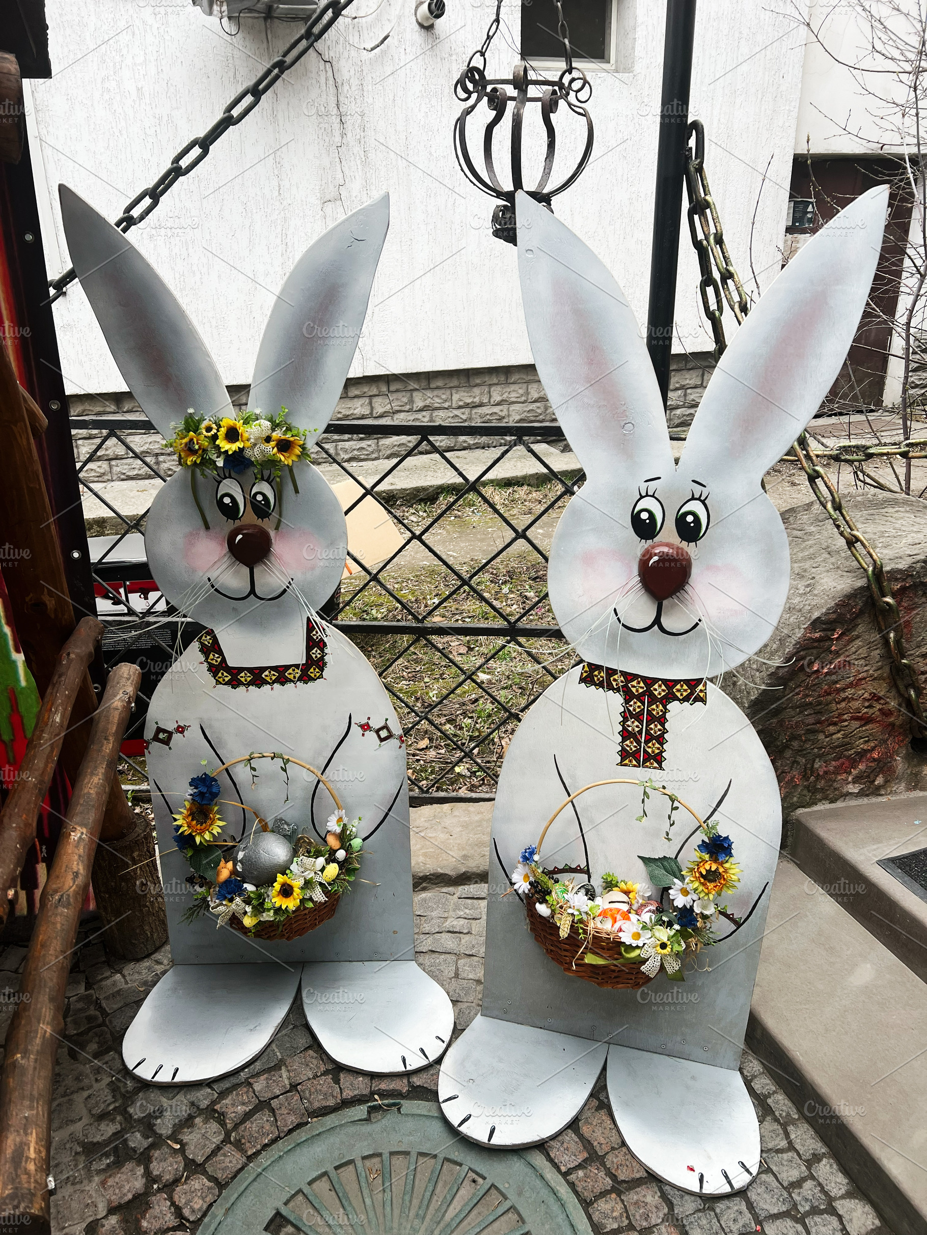 Decorative bunny figures holding festive baskets with flowers and eggs in sprin, a Photo by AS photostudio