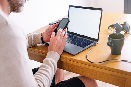 Man working from home on a laptop and smart phone sitting at a desk surfing the, a Person Photo by karrastock