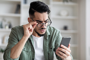 Eyesight Problems Concept. Young Arab Man In Eyeglasses Looking At Smartphone S, a Photo by Prostock-Studio