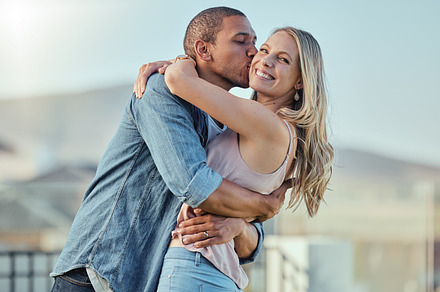 Interracial man and woman, love and kiss outside feeling happy, in love and caring in the city. Romance, romantic and boyfriend and girlfriend embracing, hugging and kissing with affection in town, a Photo by Peopleimages.com
