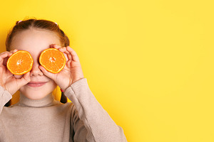 Smiling girl holding orange halves over her eyes against vibrant, a Person Photo by Ales Munt