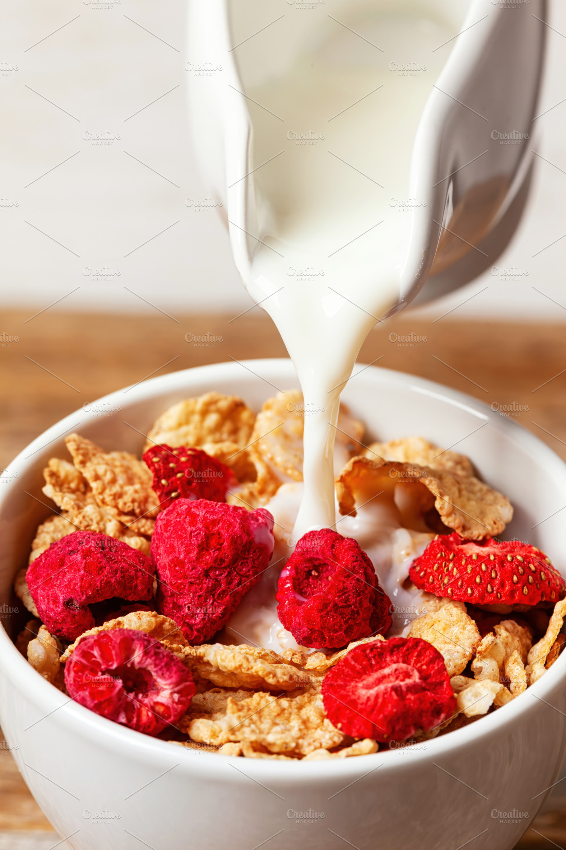 Pouring milk into bowl of cereals with dehydrated raspberries and strawberries, a Food & Drink Photo by Antonio Gravante Market