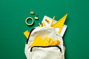 Back to school concept. Backpack with yellow school supplies on green table. Fl