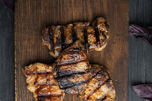 Grilled steaks on a wooden board, black background, a Food & Drink Photo by ndanko