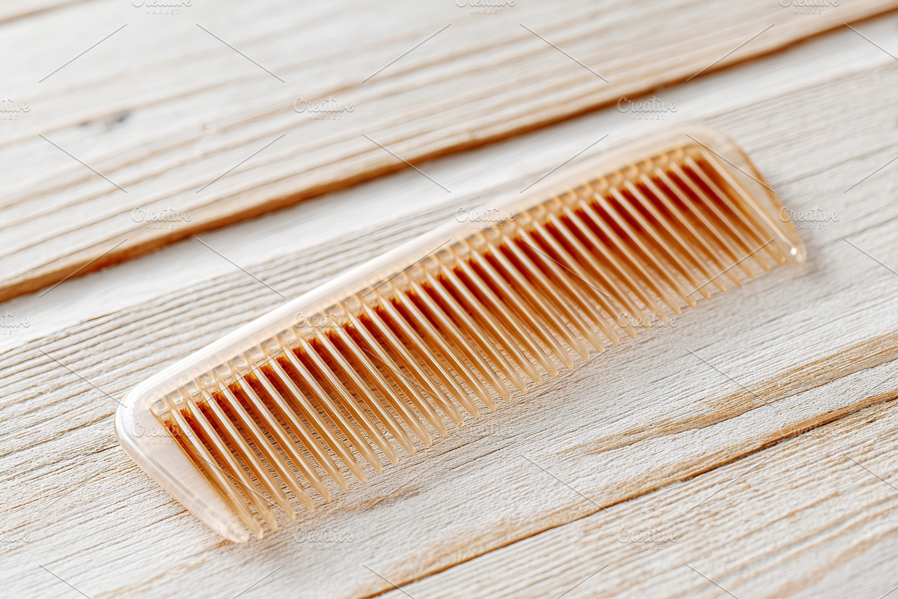 Fine-toothed plastic comb resting on a textured wooden surface in a bright sett, a Photo by AlyaAnd