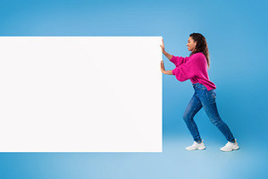 Full length of young African American lady pushing blank white paper banner wit, a Photo by Prostock-Studio