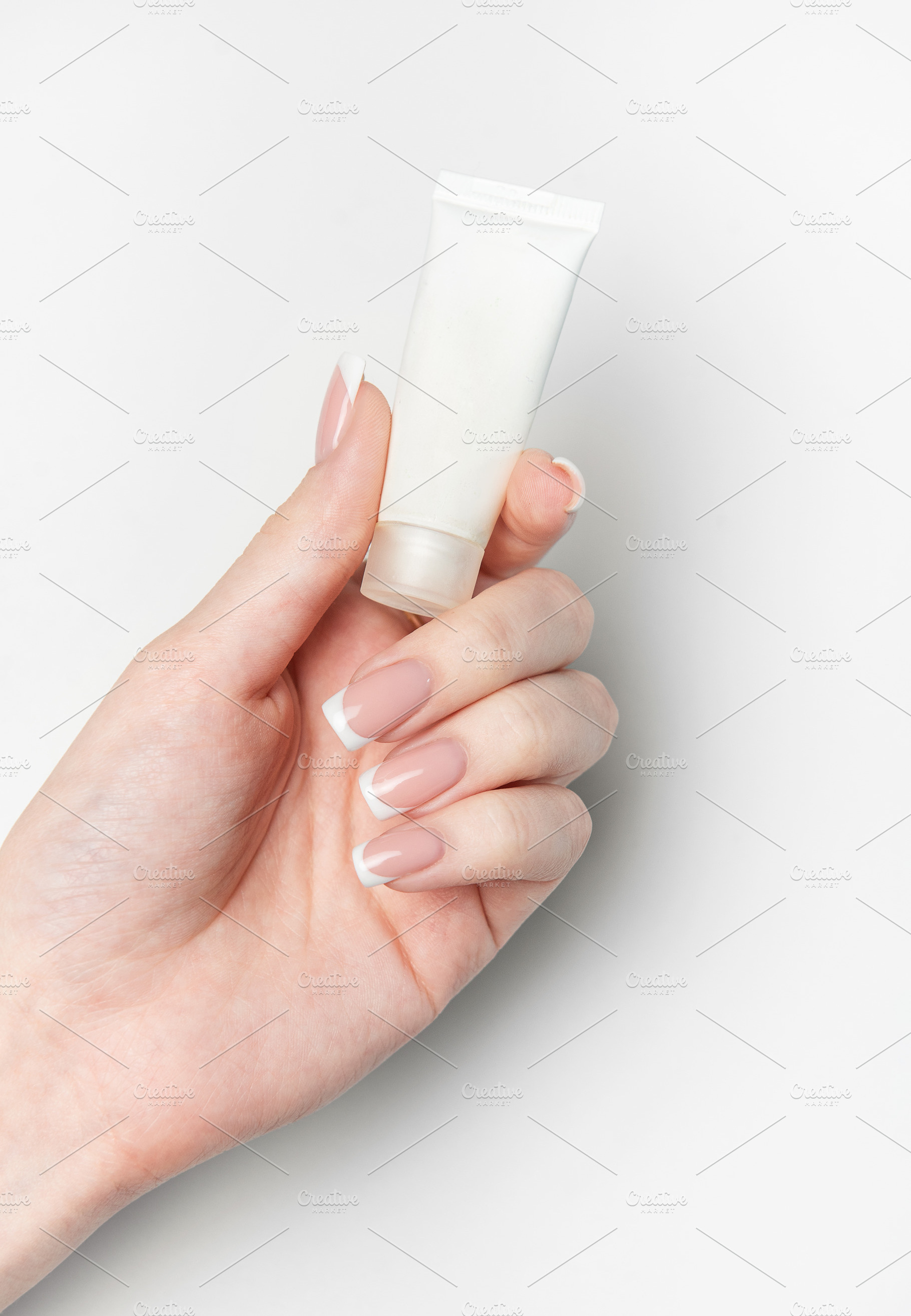 Woman hand holding white cosmetic tube on white background, a Beauty & Fashion Photo by Olena Rudo