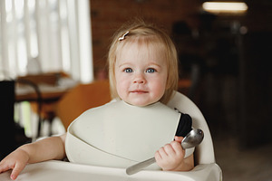 Infant girl or toddler sitting on high chair. Eating food by herself using spoo, a Person Photo by Lenor4ik