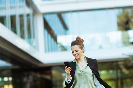 female employee in business district using phone and walking, a Business Photo by Alliance Images