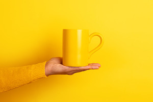 Hand in yellow sweater presenting a plain yellow ceramic mug on, a Food & Drink Photo by Ales Munt