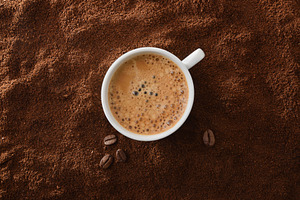 Cup of frothy coffee in center over ground with beans, a Food & Drink Photo by Davizro's Market