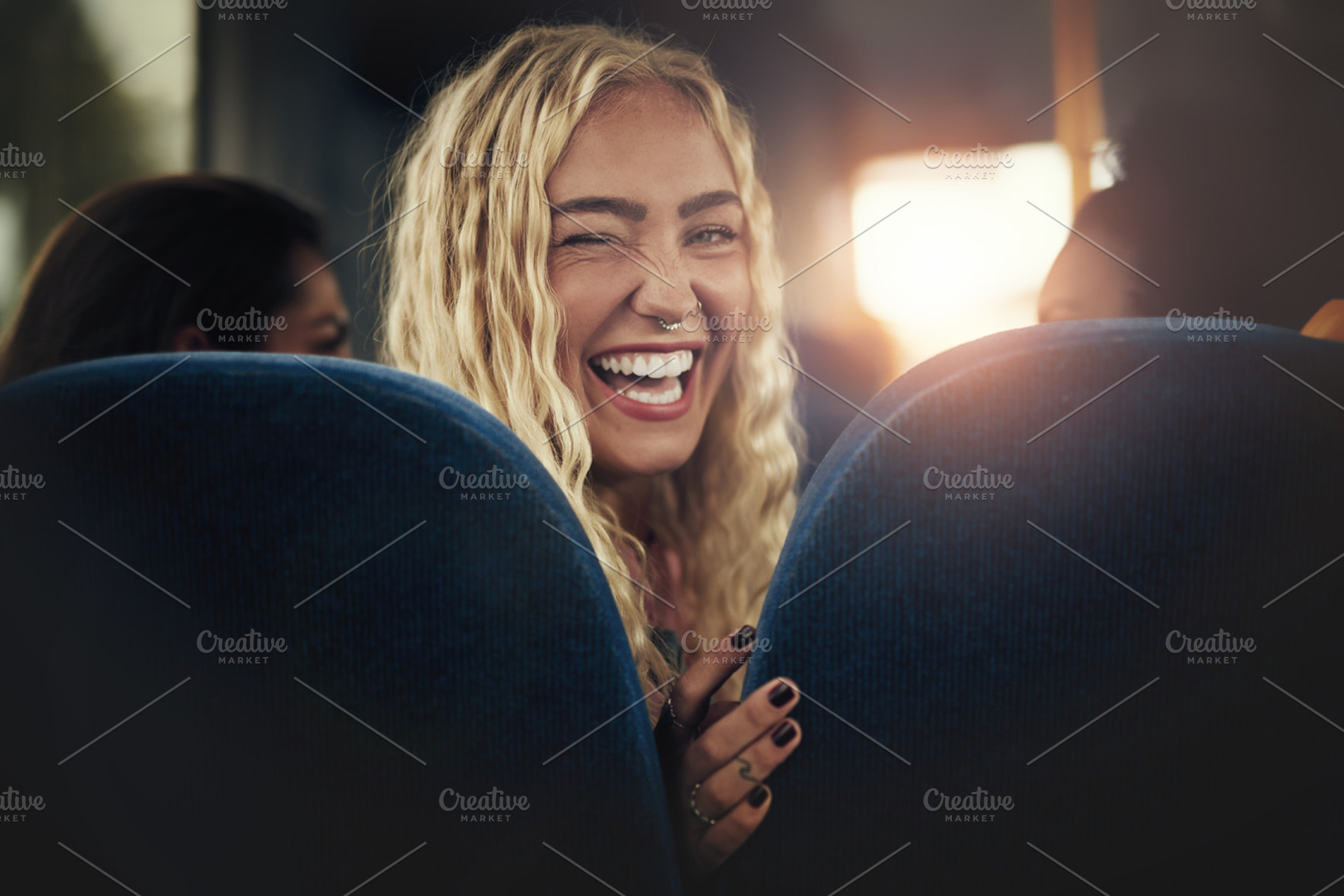 Young woman laughing and winking while sitting on a bus containing adults, a Person Photo by Stefan & Janni