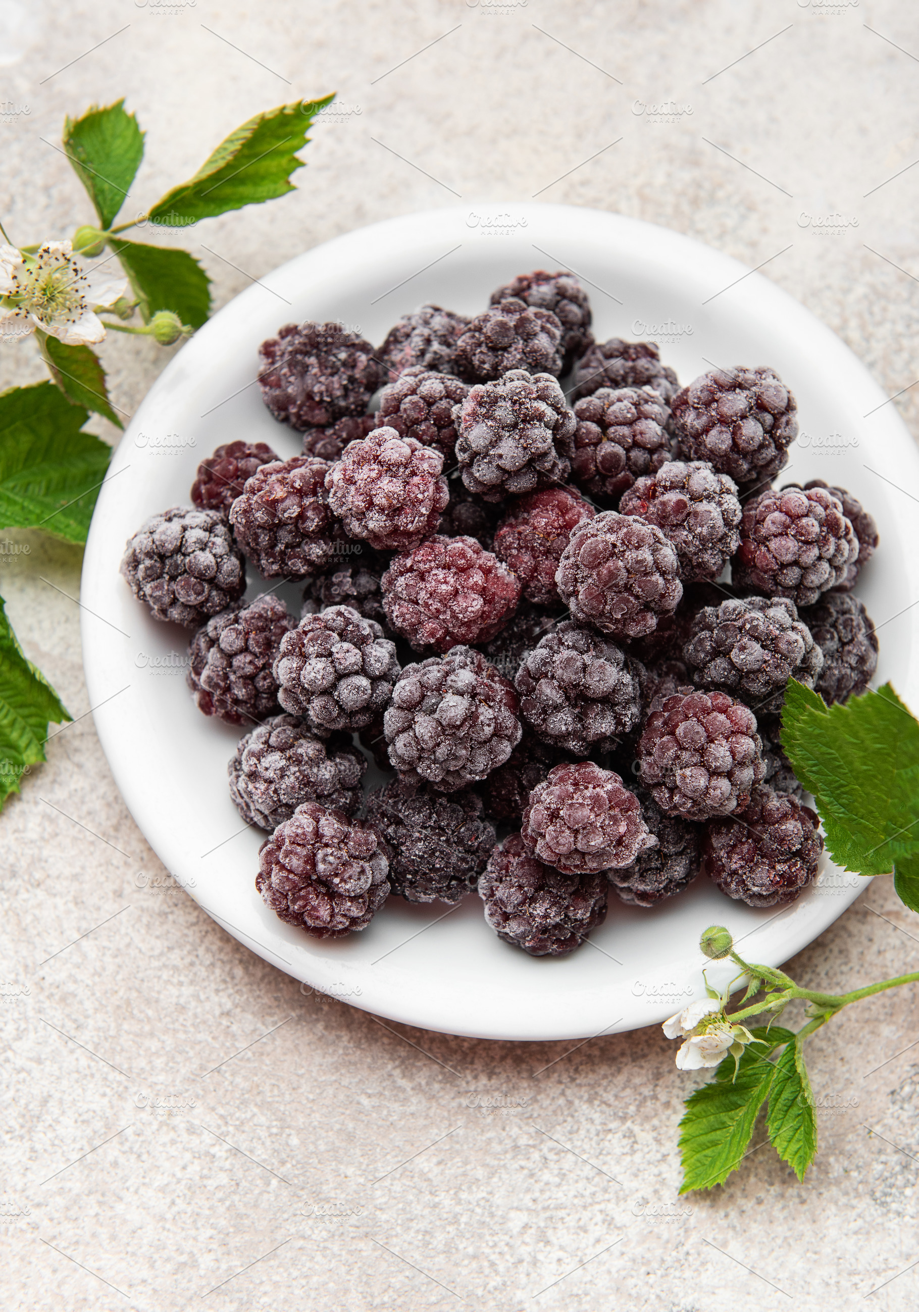 Frozen blackberries on white plate with fresh leaves, a Food & Drink Photo by Olena Rudo