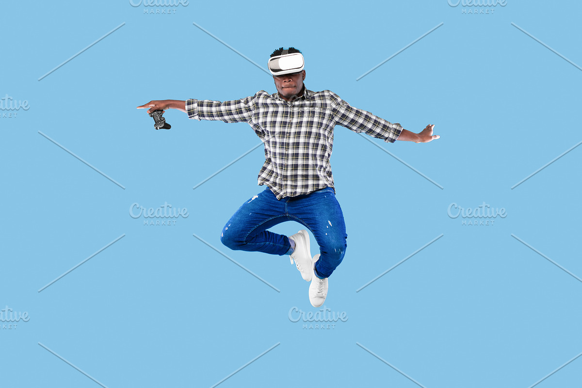 Young African American guy in VR headset holding joystick, jumping up in air on, a Photo by Prostock-Studio (Photo 1 of 2)