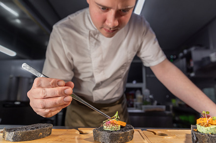 Chef placing microgreens on gourmet black bread canapes, a Photo by Grafvision photography
