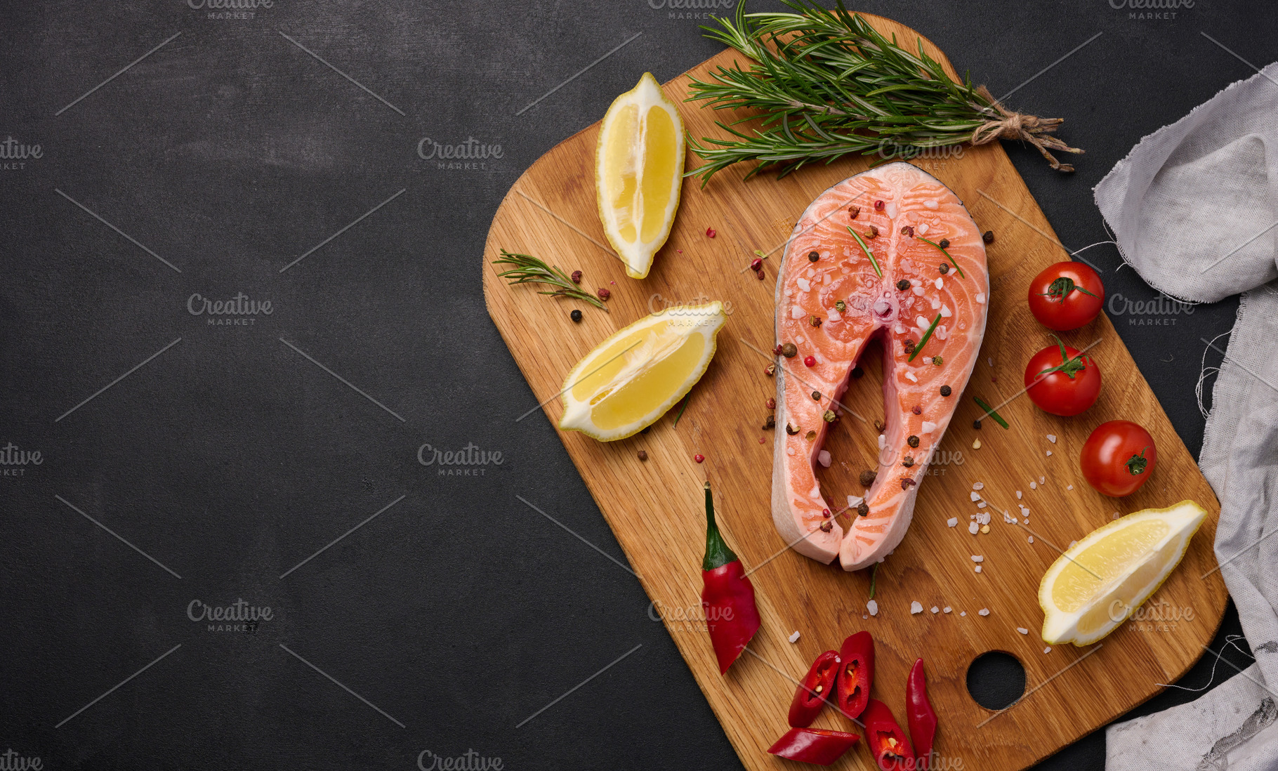 Raw salmon steak on a wooden cutting board, lemon slices, spices, a Food & Drink Photo by ndanko