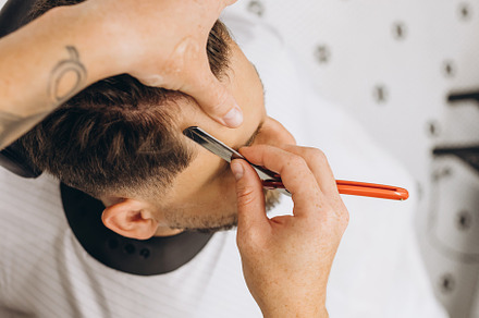 Professional barber, clipper making hair cut to customer, young man at barbersh, a Person Photo by Volodymyr Melnyk