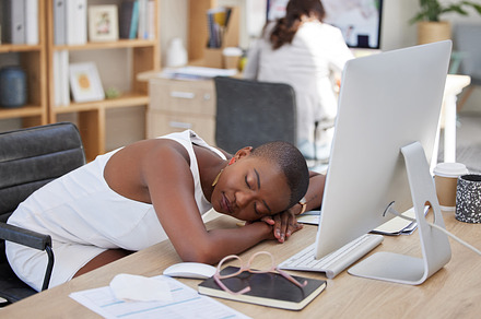 One young african american businesswoman feeling tired and exhausted from her job and sleeping on her desk in the office. Black woman resting during a break at work infront of her computer., a Photo by Peopleimages.com