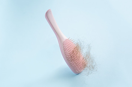 Hair loss concept - pink brush with lost hair on blue background