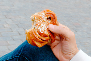 a man holds a bitten kanelbulle in a public square, a Photo by Nito