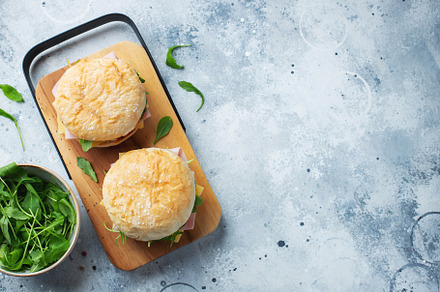Two homemade sandwiches with ham, cheese and arugula on a concrete table., a Food & Drink Photo by Budarinphoto