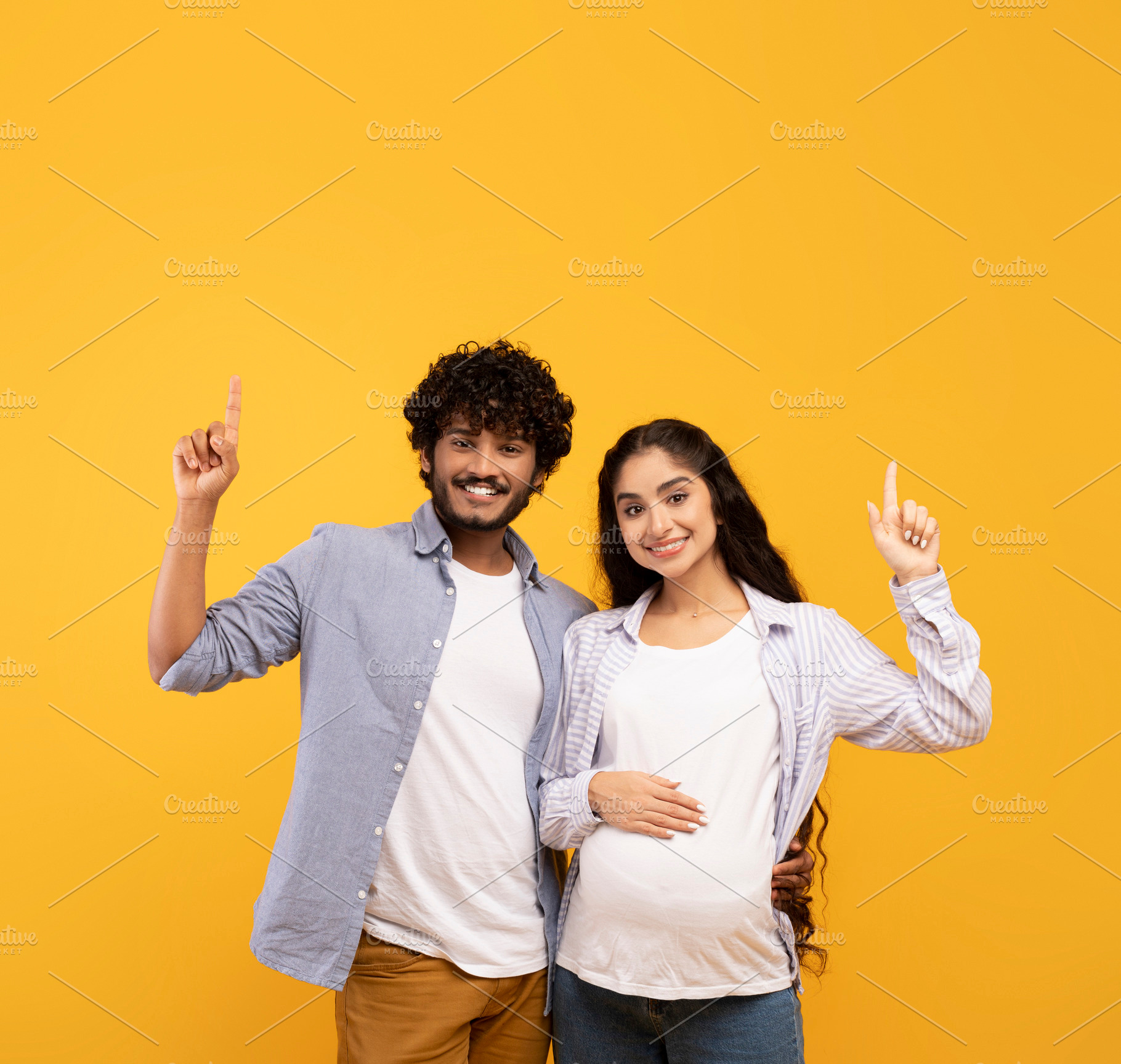 Excited indian pregnant lady and her husband pointing up at free space, showing, a Person Photo by Prostock-Studio