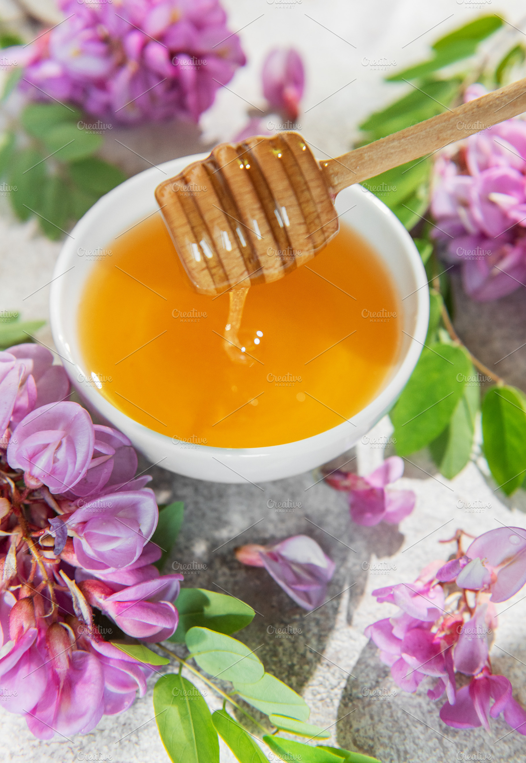 Natural honey dripping from dipper into bowl with acacia flowers, a Food & Drink Photo by Olena Rudo