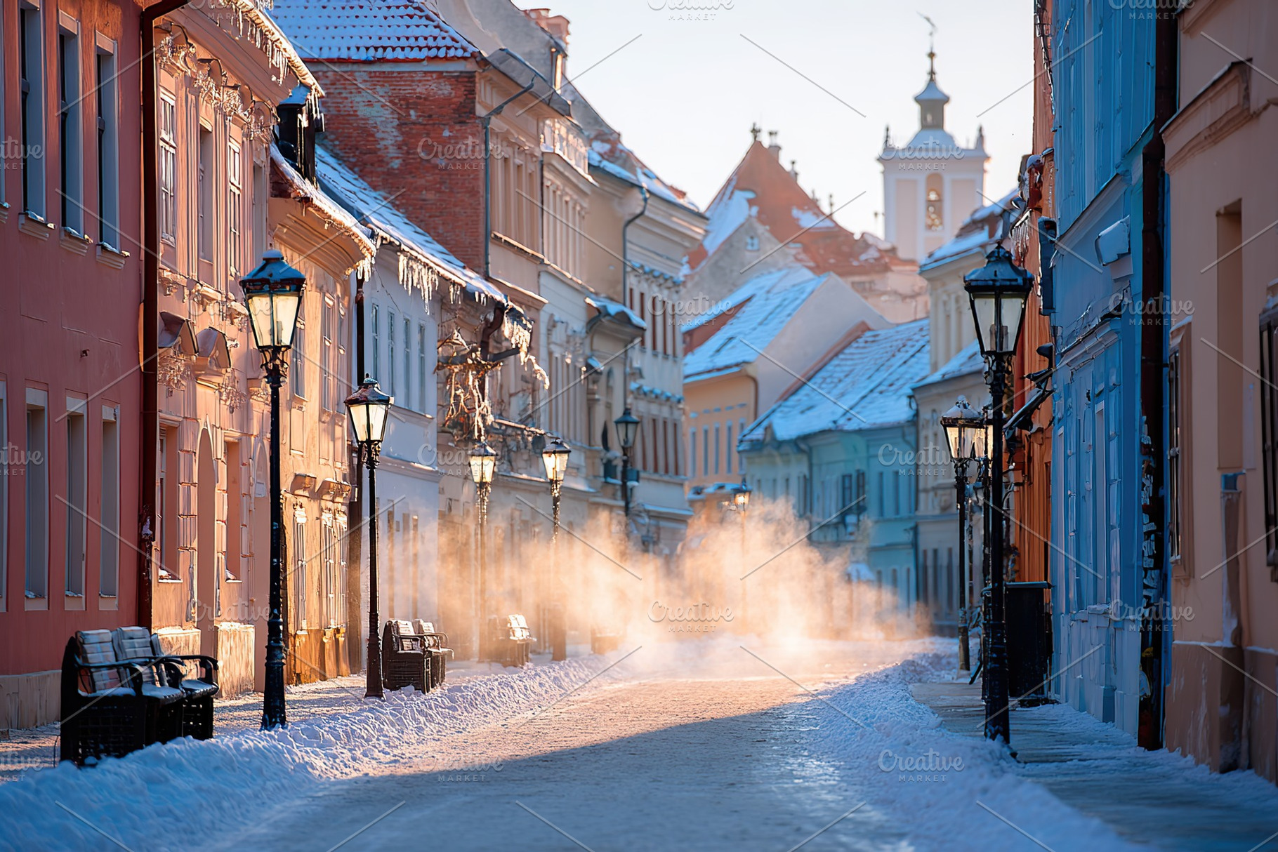 Snow-covered street in a historic town during early morning light with mist ris, a Photo by AlyaAnd