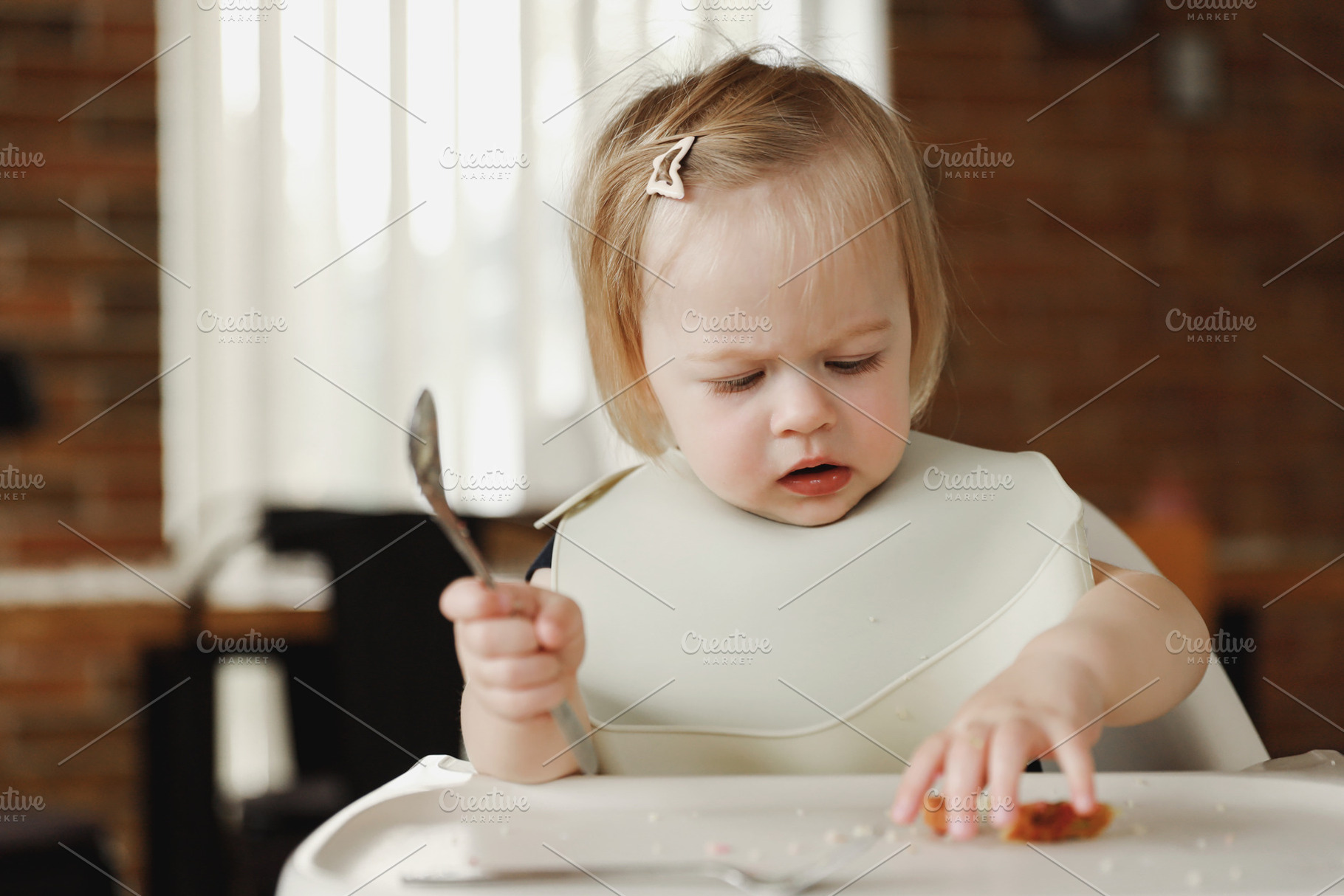 Infant girl or toddler sitting on high chair. Eating food by herself using spoo, a Person Photo by Lenor4ik