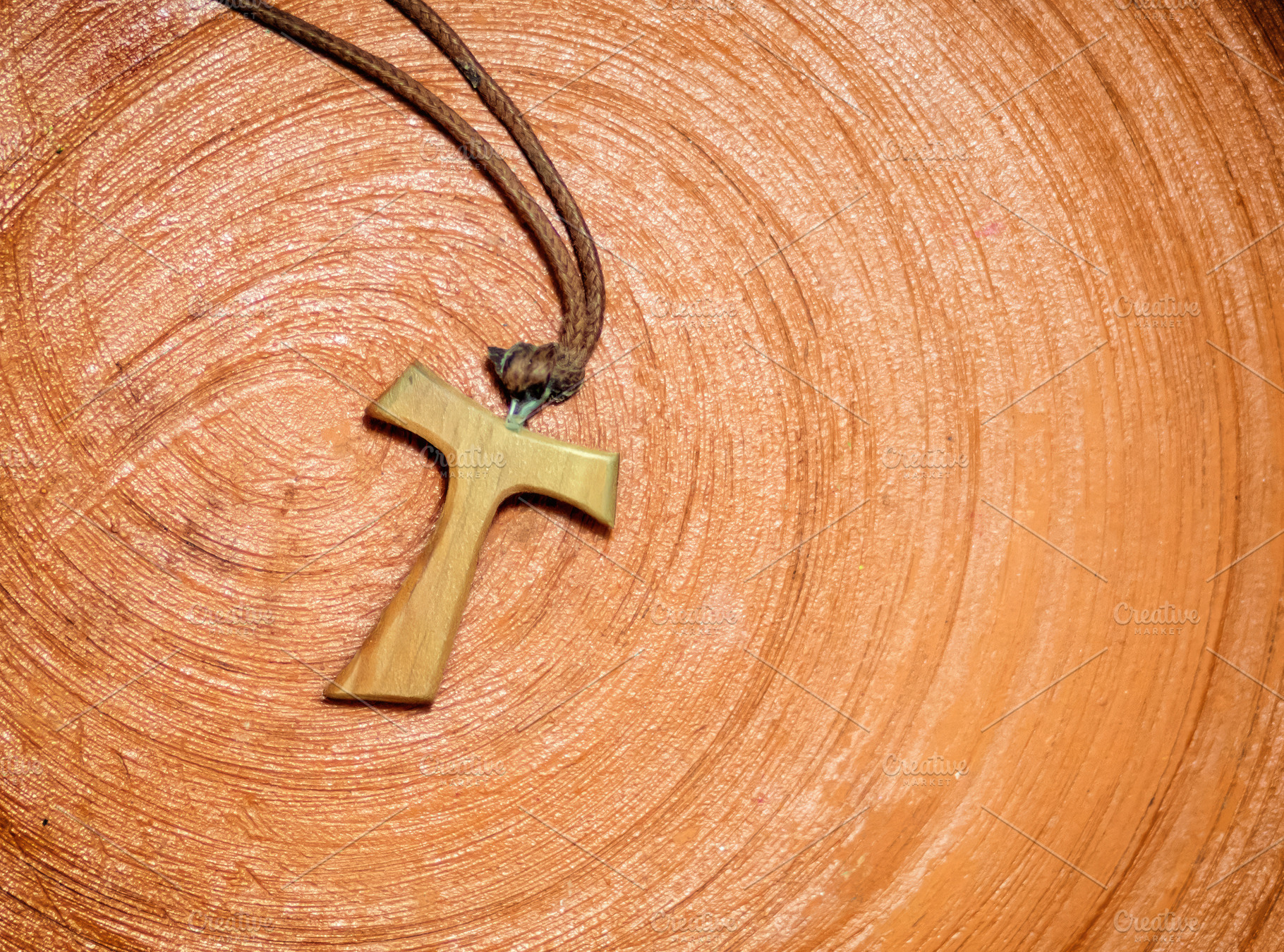 Tau cross pendant resting on a terracotta surface, a Photo by Antonio Gravante Market