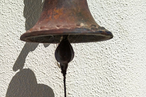 Close-up of a rustic bell casting a shadow on a white wall, an Arts & Entertainment Photo by DanFLCreativo