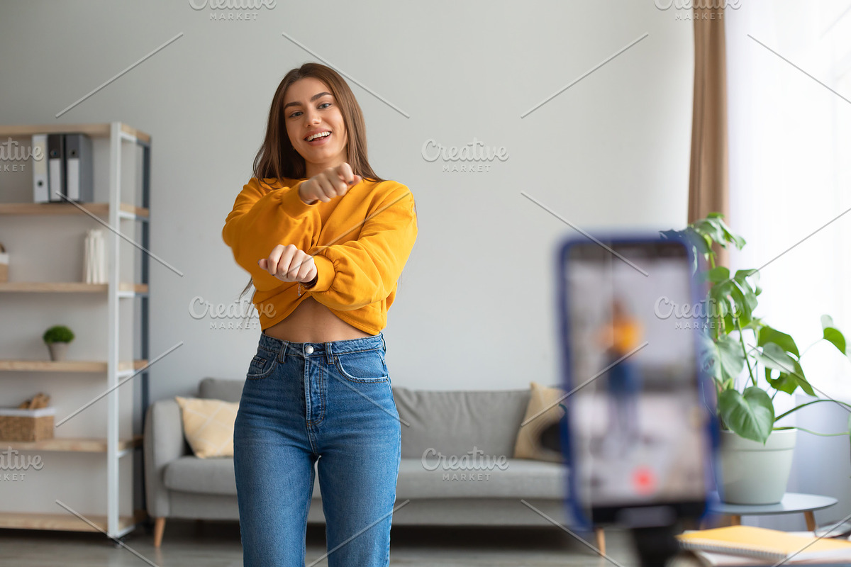 Young Caucasian female influencer recording video on smartphone, dancing on cam, a Photo by Prostock-Studio (Photo 1 of 3)