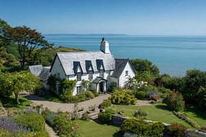 Idyllic white cottage overlooking the sea on a sunny day, with a, a Photo by Studio ANNA