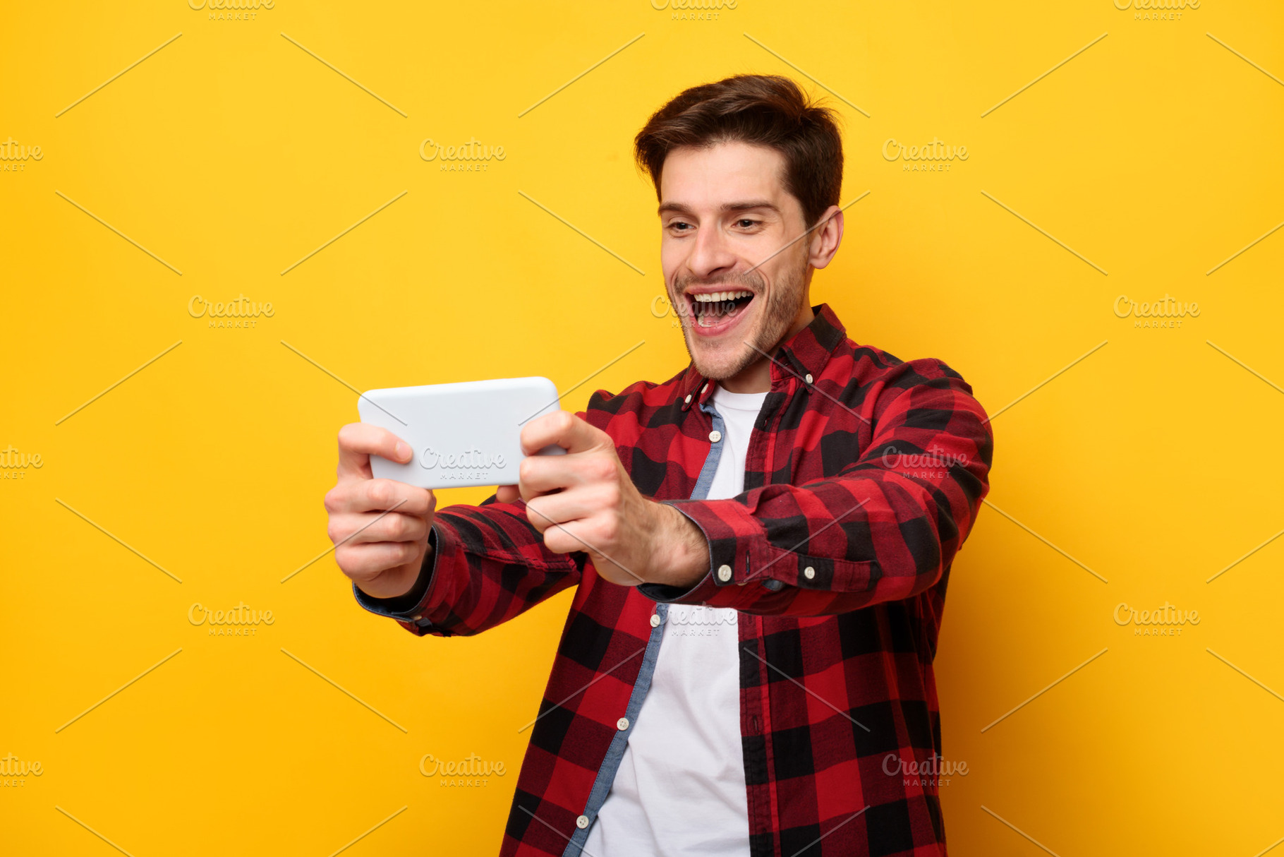 Excited man playing mobile games on yellow background, a Photo by Prostock-Studio