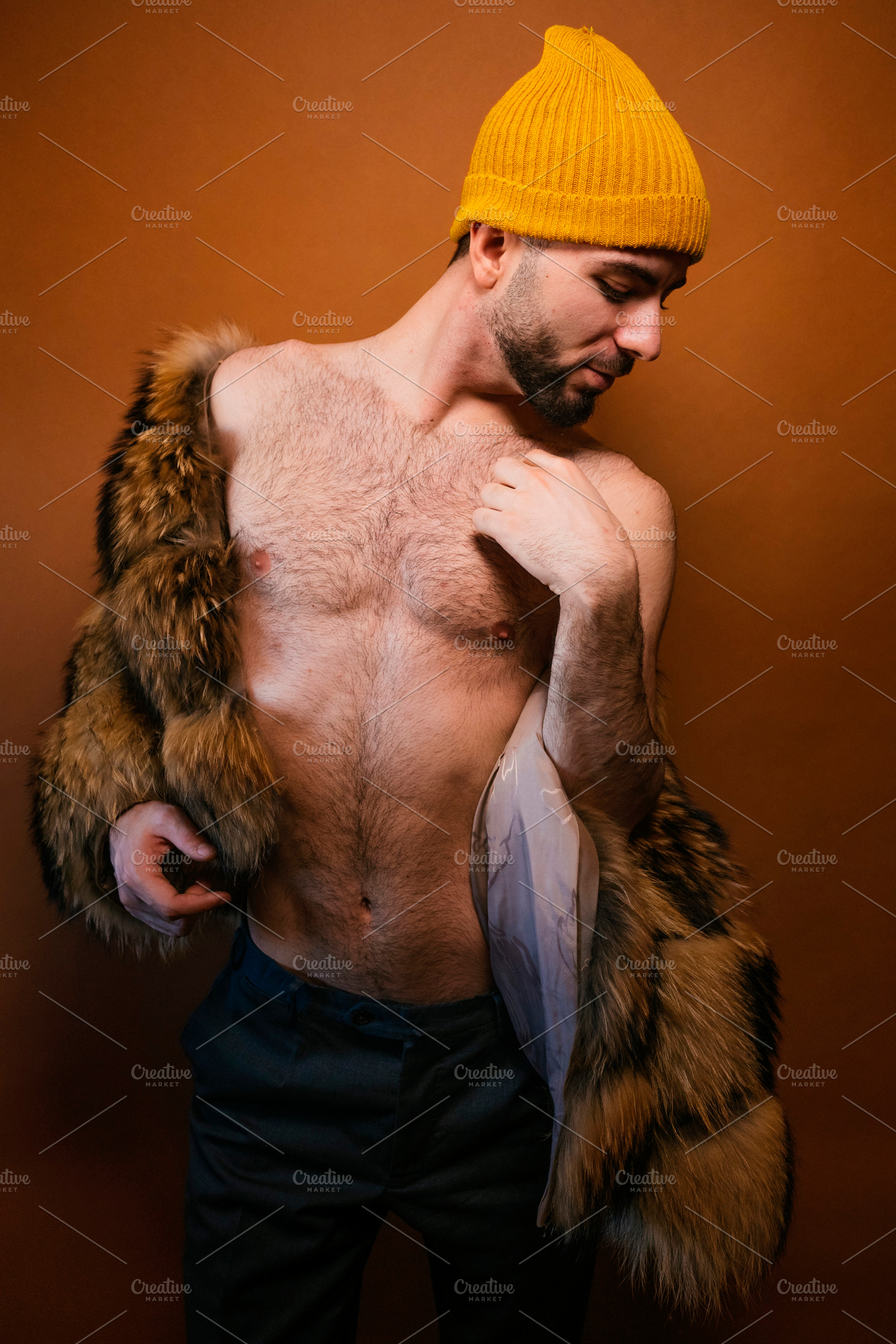 Confident man posing shirtless with fur coat and beanie, a Photo by karrastock