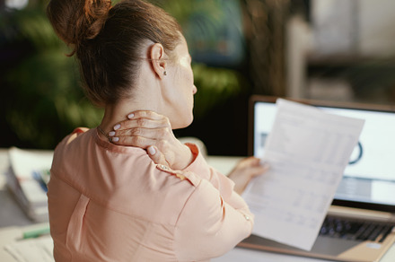Seen from behind modern woman with documents having neck pain, a Business Photo by Alliance Images