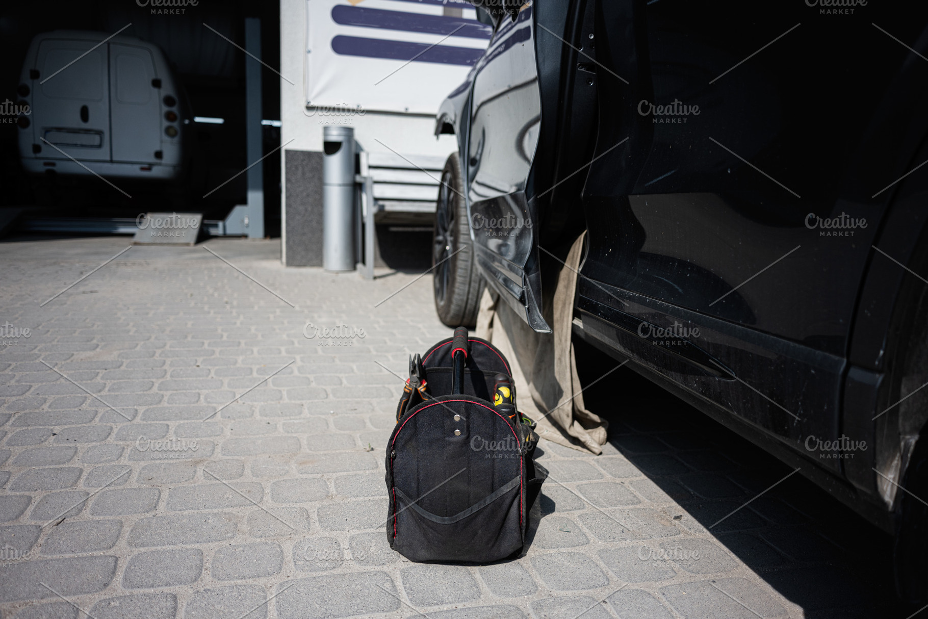 Toolbag beside a black car outdoors in a service area, a Transportation Photo by AS photostudio
