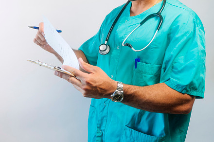 Focused male doctor reviewing documents on clipboard, wearing scrubs and stetho