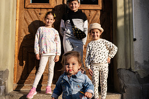 Group of four children posing outdoors on a sunny day by a wooden door, a Person Photo by AS photostudio